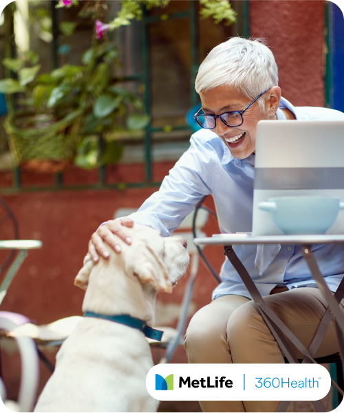 Lady sitting outside at a cafe on her laptop, patting a dog