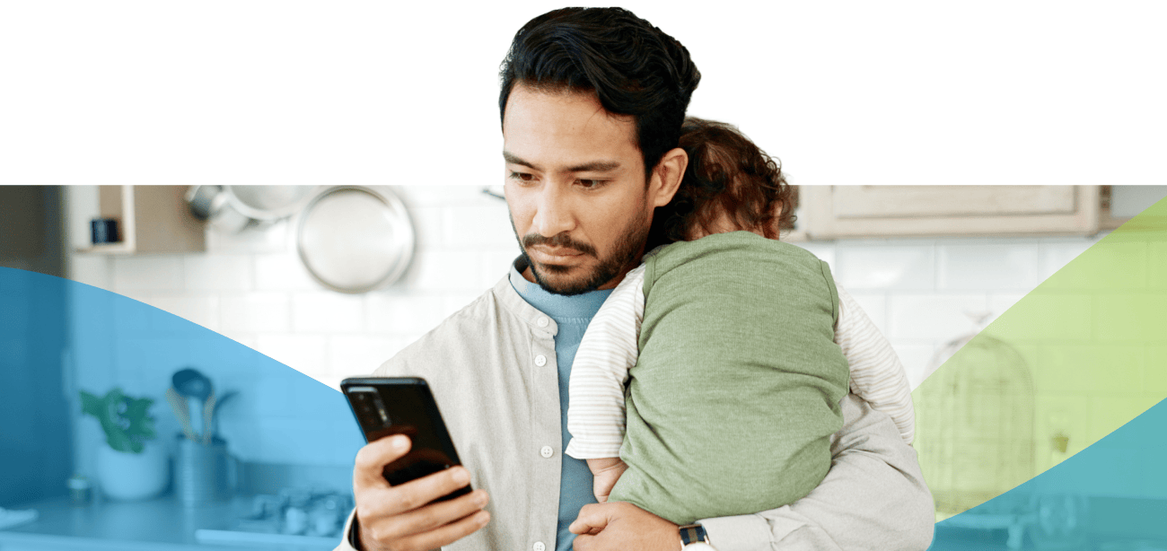 Young man on his phone while holding a baby