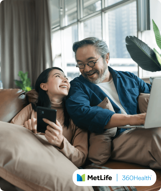 Two people smiling on a couch, using a laptop and smartphone.