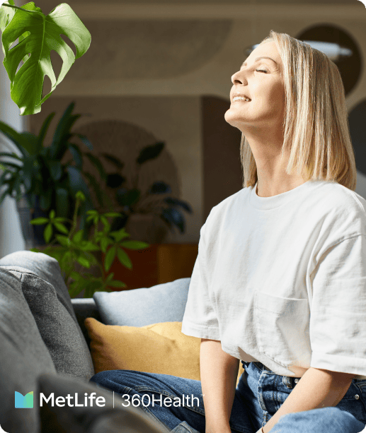 Person sitting on a couch near a window with plants, eyes closed, in soft natural light