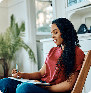 Woman sits at home writing in a journal.